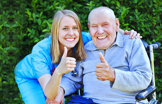 caregiver and senior man are smiling while doing a thumbs up together